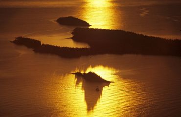 Aerial view of a collection of forested islands with sunlight shimmering over the surrounding water.