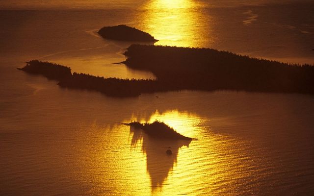 Aerial view of a collection of forested islands with sunlight shimmering over the surrounding water.