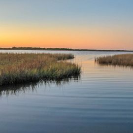 An expanse of dense coastal wetlands intermixed with open water along the Texas Gulf Coast at sunset; the sky is orange.