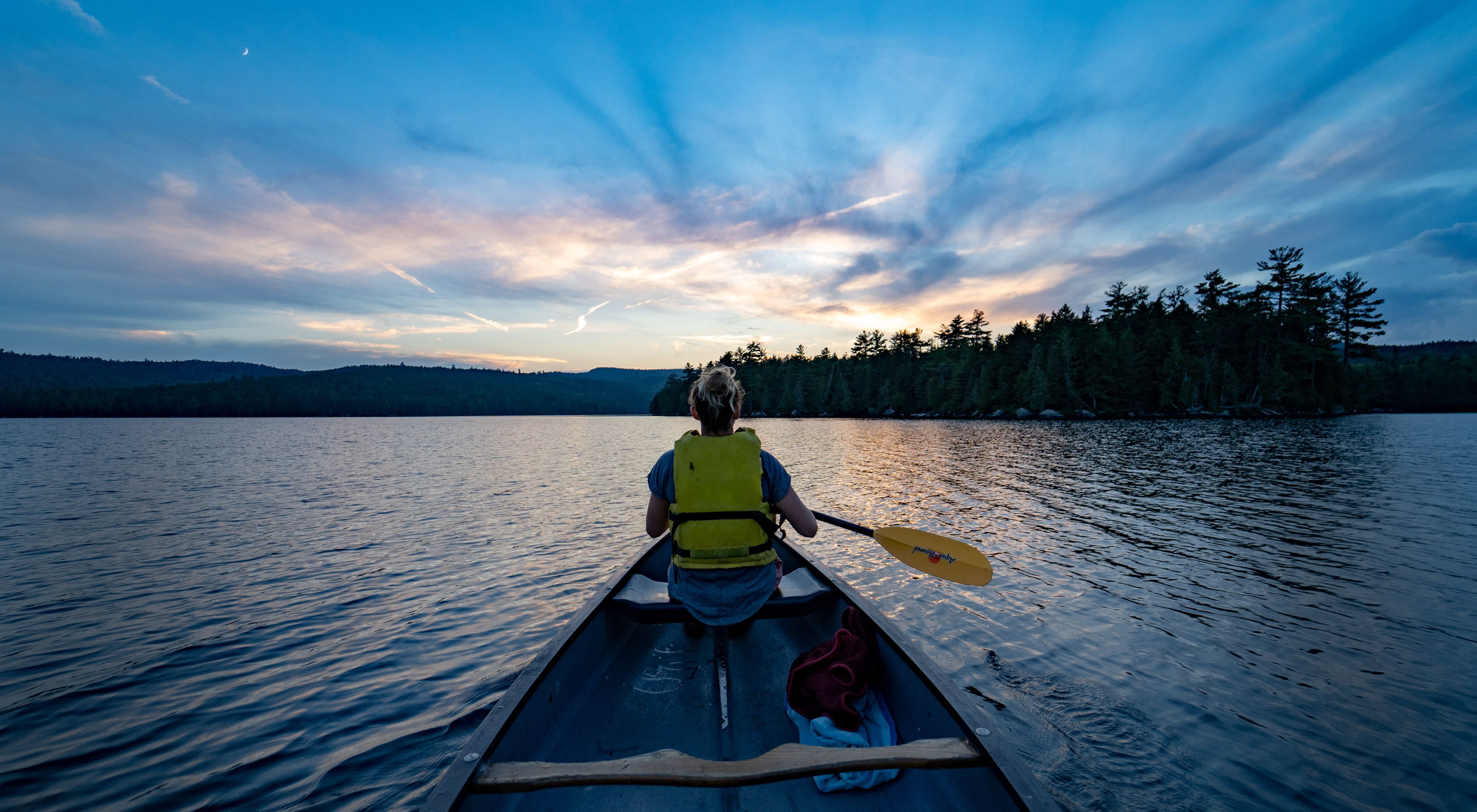 View from the stern of a canoe as the boat moves toward the setting sun.