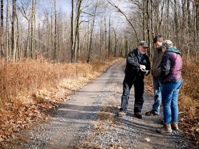 Three people stand together on the edge of a gravel road that extends into the horizon behind them.