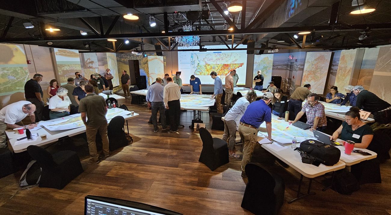 Several people gather to examine information presented on tables.