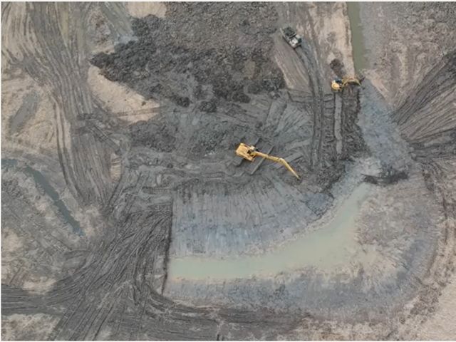 An aerial view of construction vehicles working in a very muddy area. 