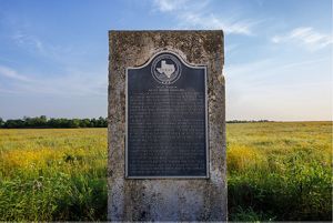 A historical marker made of stone in a field of grass.