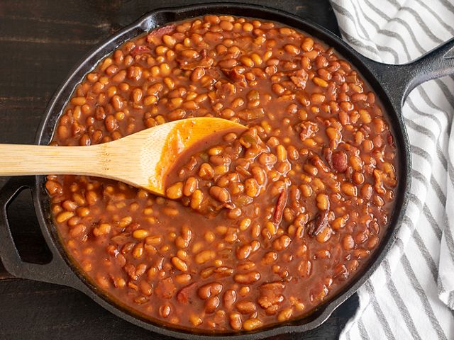 Baked beans in a skillet. A wooden spoon rests on top of the dish.