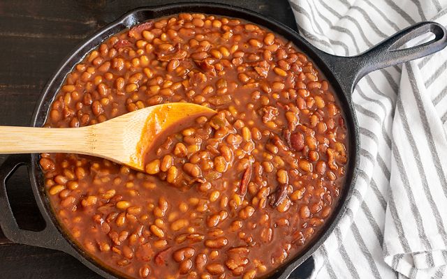 Baked beans in a skillet. A wooden spoon rests on top of the dish. 