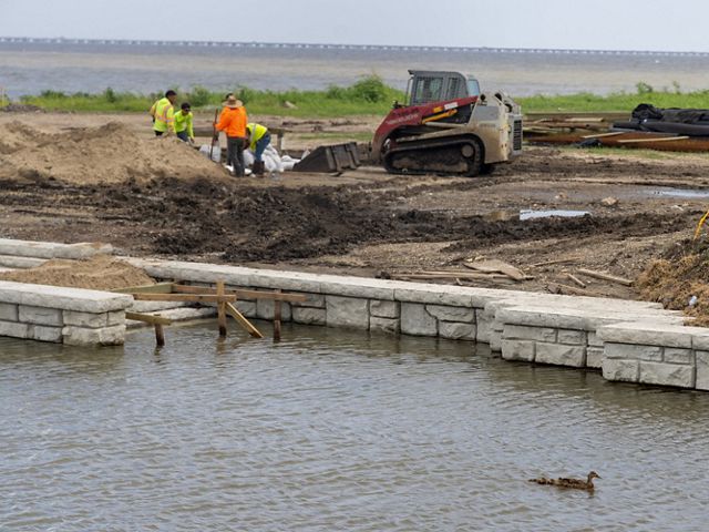 A group of men work near a small bulldozer at a construction site along a river.