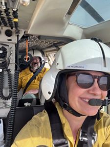 Two crew members facilitating the controlled burn fly in a helicopter wearing helmets and smiles.