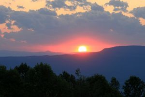 An orange and pink sunset over mountains and trees at dusk.