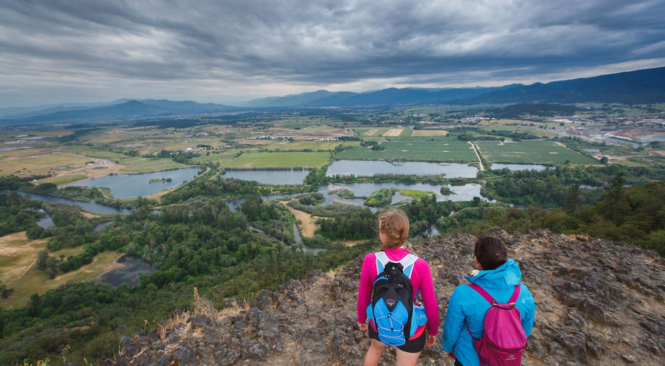 Two people standing on a rock outcrop looking out over forests and farms.
