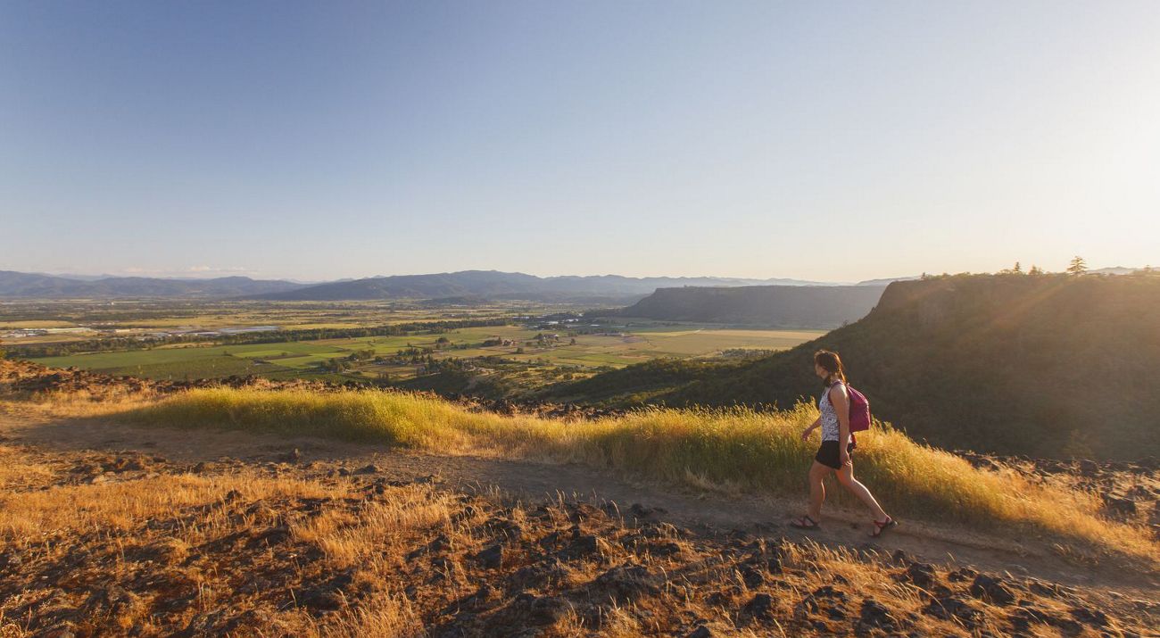 A woman hikes along the edge of Upper Table Rock overlooking the Rogue Valley at sunset, Oregon.