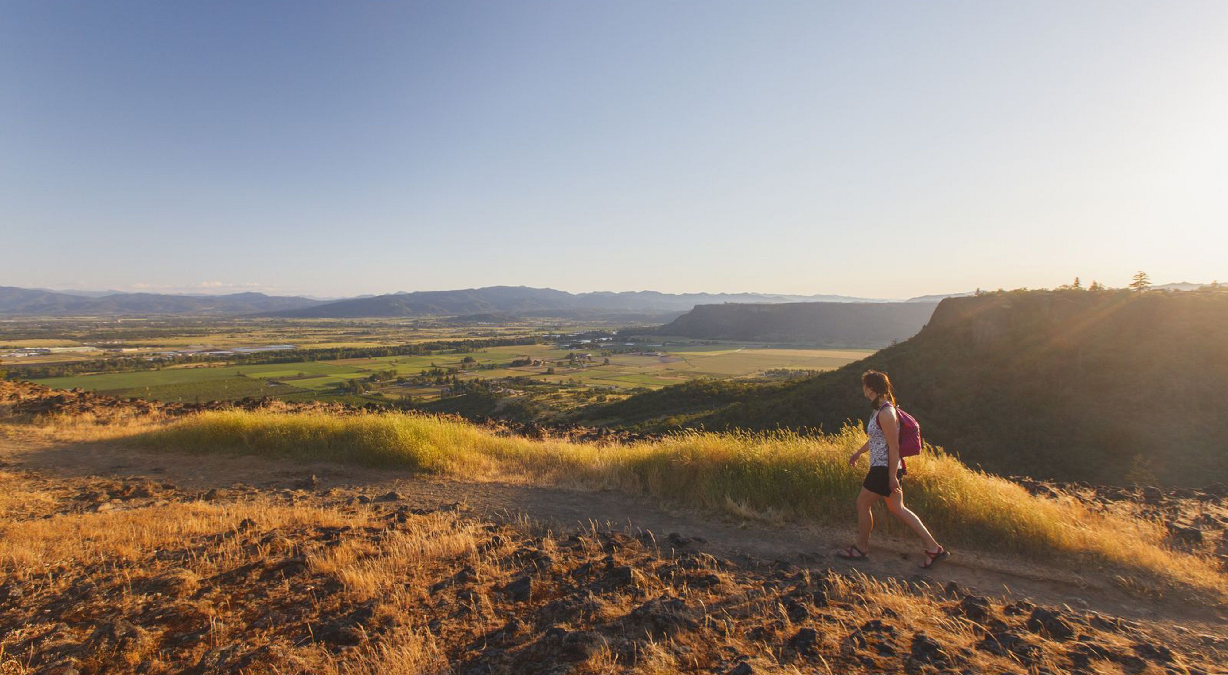 A woman hikes along the edge of Upper Table Rock overlooking the Rogue Valley at sunset, Oregon.