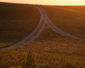 Sun sets on open prairie with two trails merging on a hilltop.