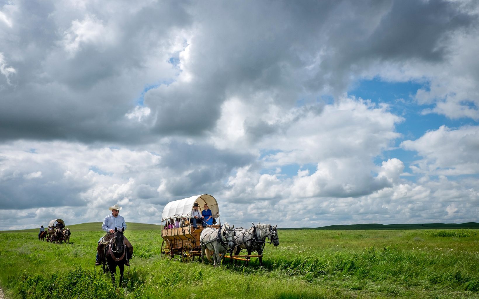 People in covered wagons pulled by horses in a vast open grassland.