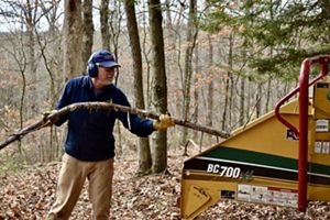 A man feeds a long, thin tree branch into a large wood chipper.