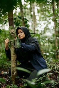 A woman fixing a camera onto a tree.