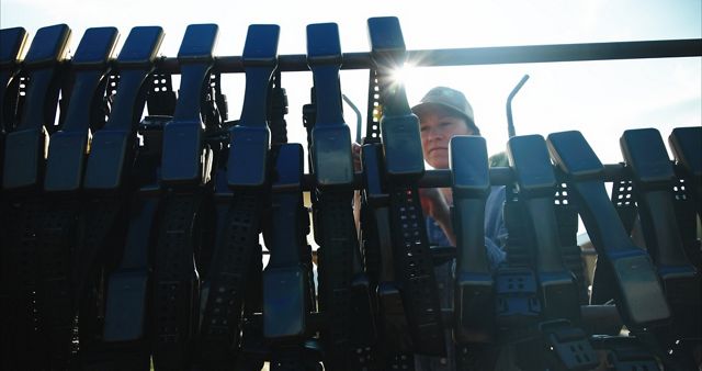 A woman wearing a hat stands behind a fence with more than a dozen black cattle collars lining it.