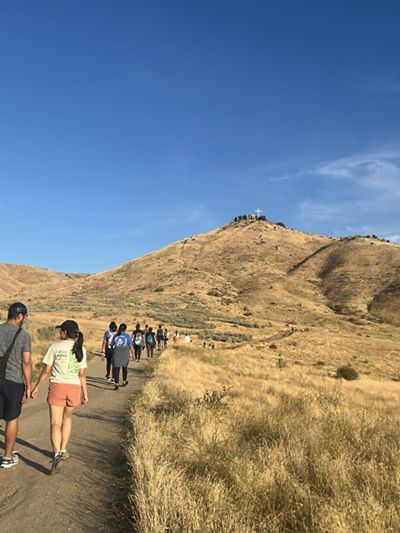 People hike on trail that winds through a grassy landscape.