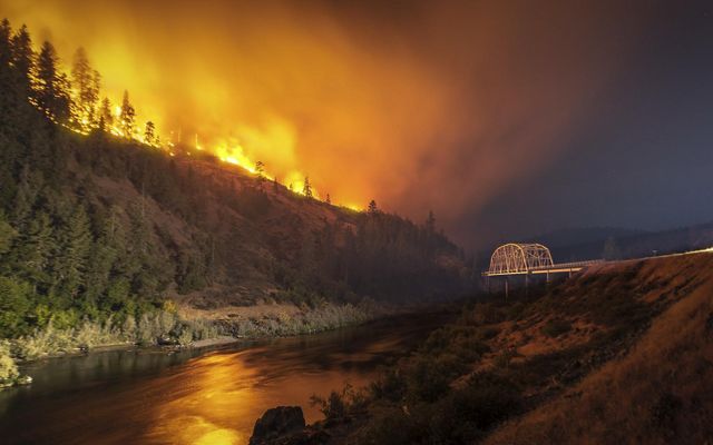 Photo of wildfire at night burning near Rogue River and Hellgate Bridge in Oregon.