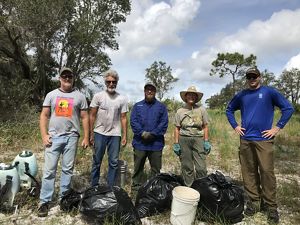 Five volunteers stand with smiling faces as they reflect on the hard work it took to create the many full bags of natal grass at their feet.