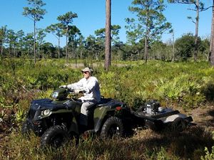 A volunteer on an ATV pulls a mower behind them to perform trail maintenance. 