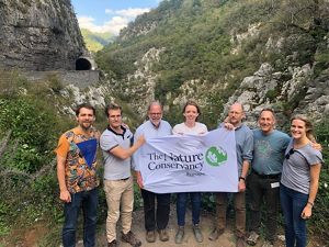 Seven people stand before a gorge holding a TNC banner.