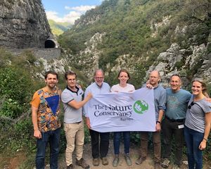 Seven people stand before a gorge holding a TNC banner.