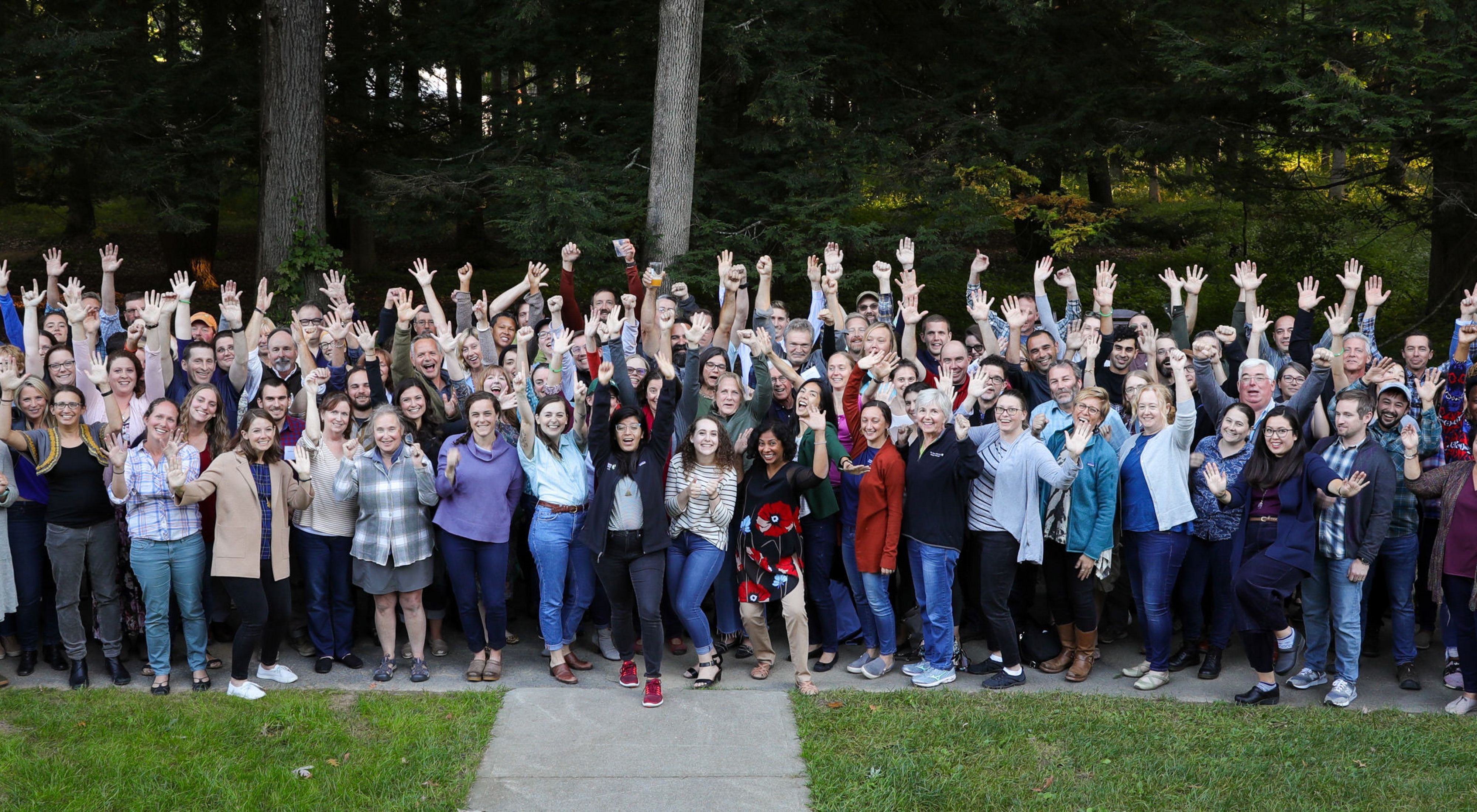 Group picture of TNC staff in an outdoor setting smiling at camera with arms raised.