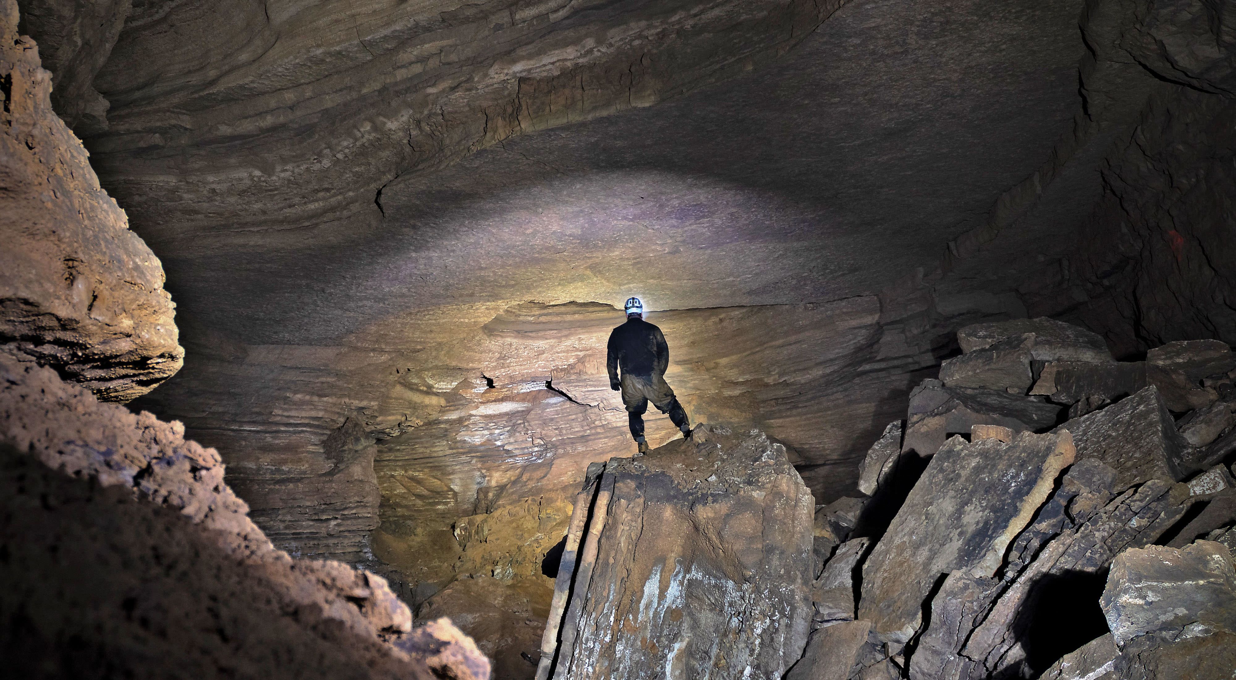 A man stands at the bottom of a large cave.
