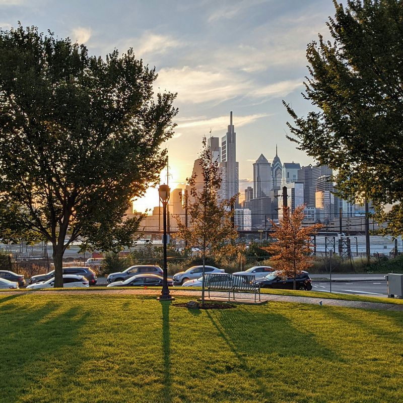 A park at sunset with the Philadelphia skyline in the background.