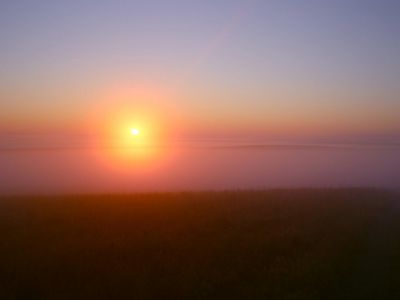 The sun rises over a hazy horizon.