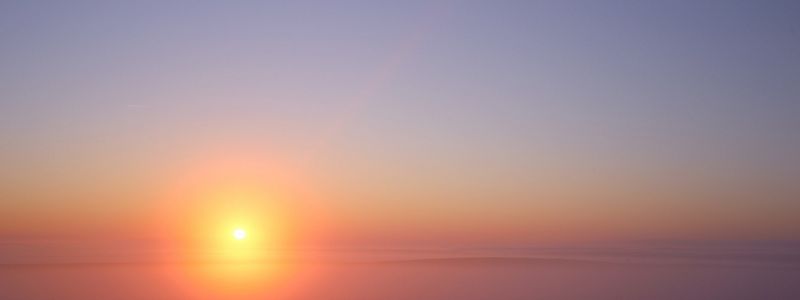 The sun sets over a hazy horizon.