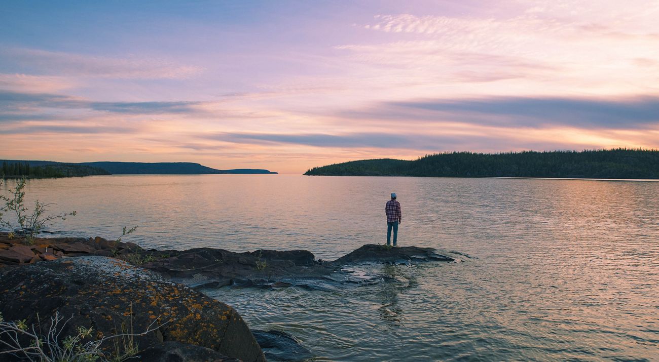 A man stands on a small island overlooking Christie Bay at sunset.