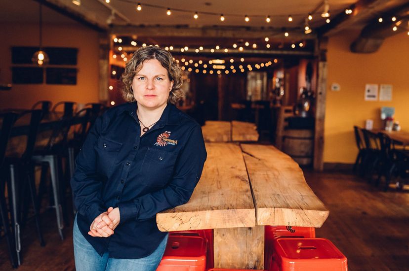 Throwback Brewery Co-Founder Nicole Carrier leans against a wooden table inside the brewery.