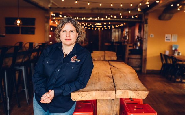 Throwback Brewery Co-Founder Nicole Carrier leans against a wooden table inside the brewery.