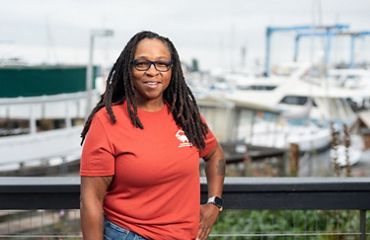 Candid portrait of Tia Clark standing at a dock with boats in the background.