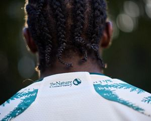 A person with their back facing the camera showing the TNC logo on the back of their shirt collar.