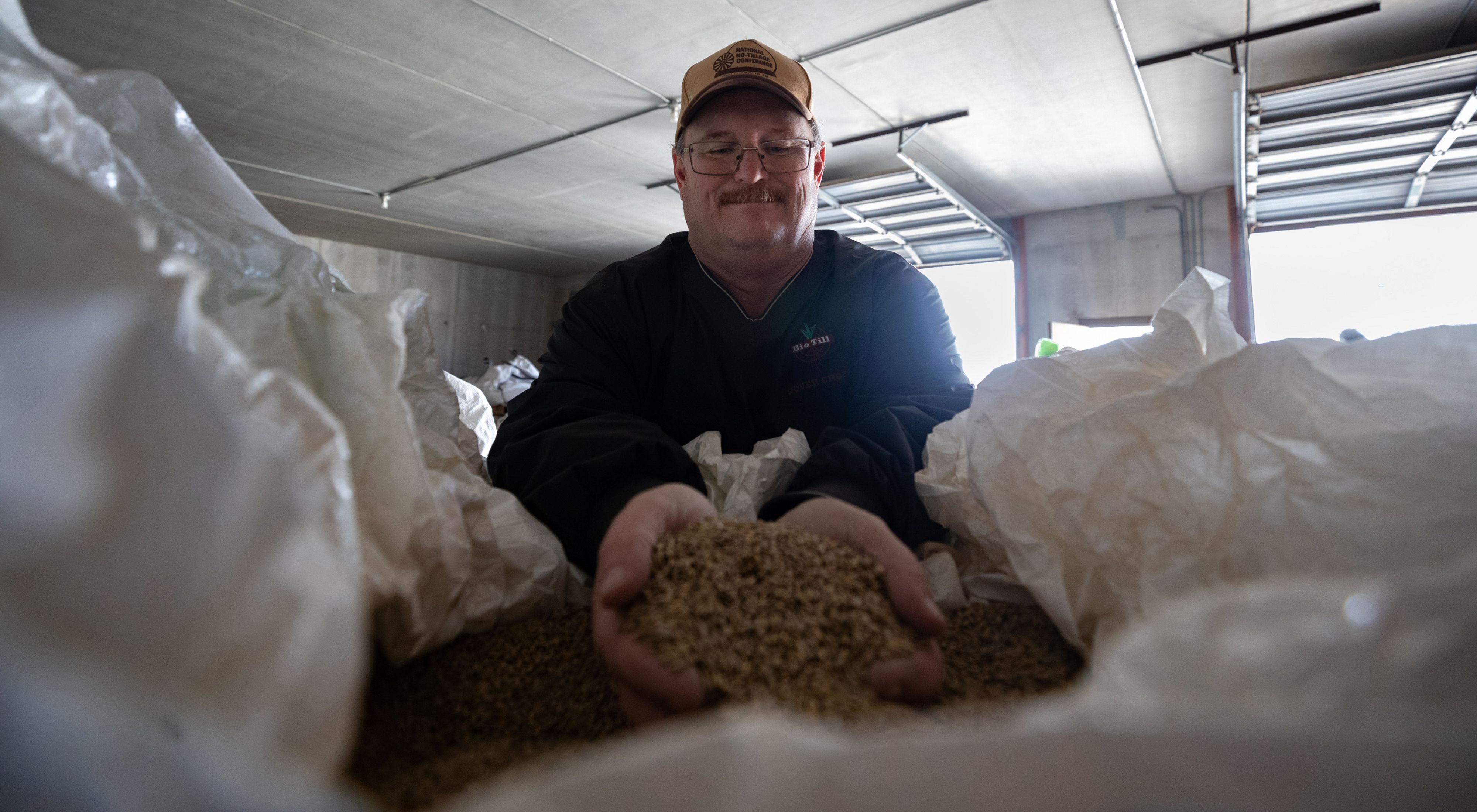 A smiling ag retailer inspects a bag of cover crop seed, ready for planting.