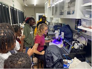 Students listen and look as a scientist teaches them about microscopes and how the tool is used to observe coral growth and spawning. 