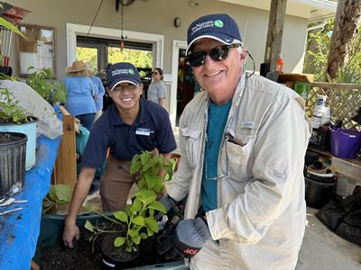 Two people pose around a potted plant in a plant nursery.