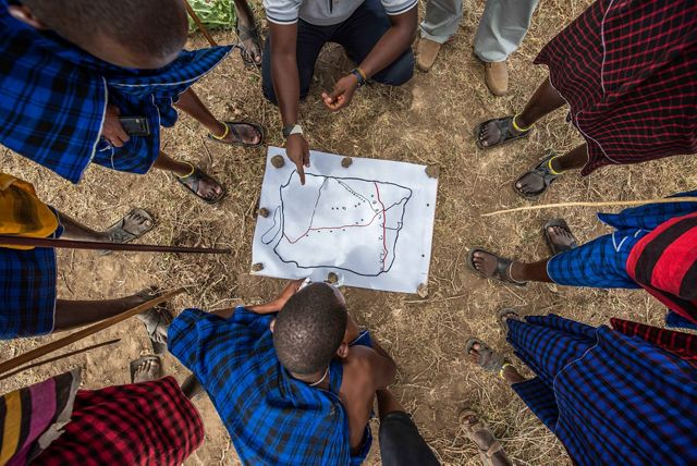 Photo of a ring of people in northern Kenya looking down at a hand-drawn map on the ground.