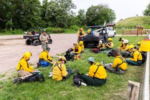A group of people dressed in yellow clothing sit in a grassy area to read materials and meet.