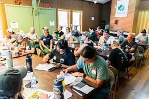 A group of women sit at tables and take notes during a class. 