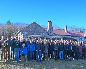 A large group of people stand together outdoors in front of a lodge.
