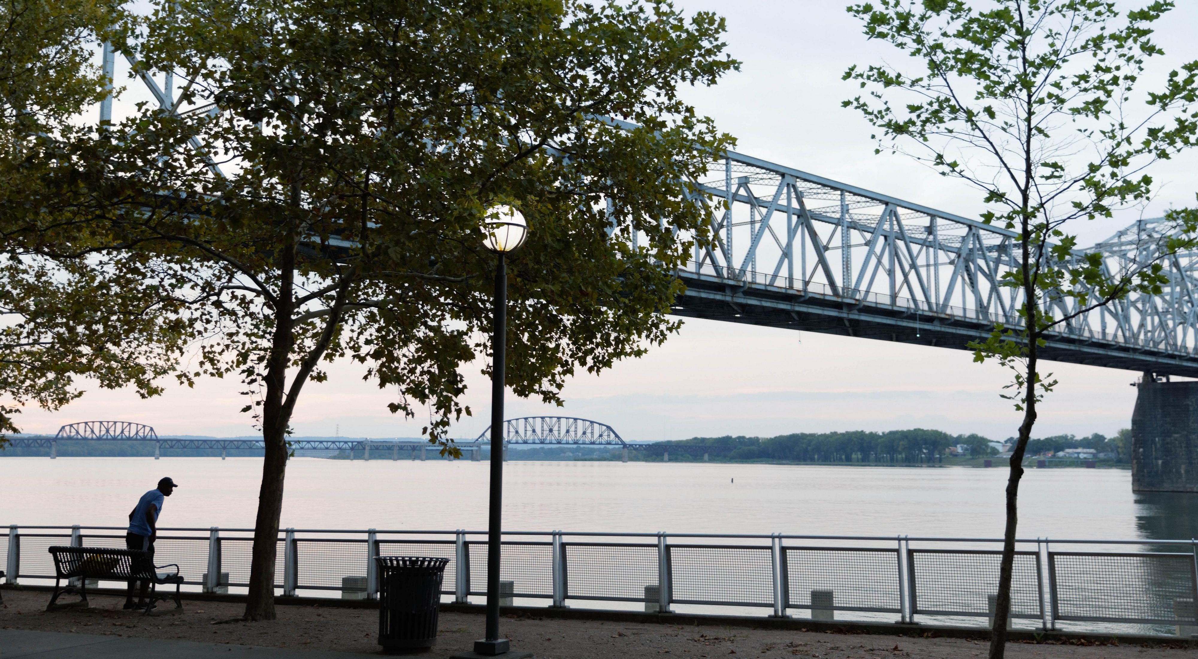 Photo of a steel bridge crossing the Ohio River, with a riverside park in the foreground.