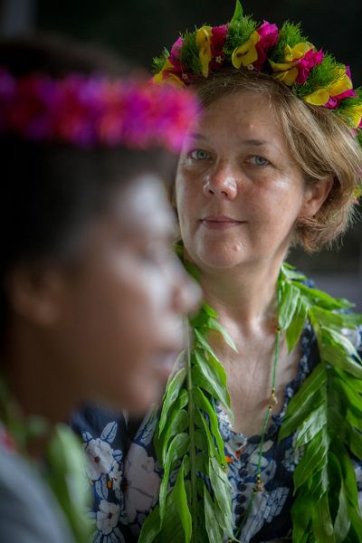 Woman wearing lei looks on in the background as woman speaks in foreground