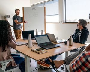A man at a white board explains his new tech company's idea.