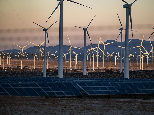 solar panels and wind turbines in front of mountains.