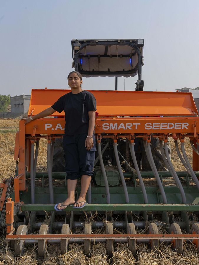 A woman stands on her seeding machine in her field.