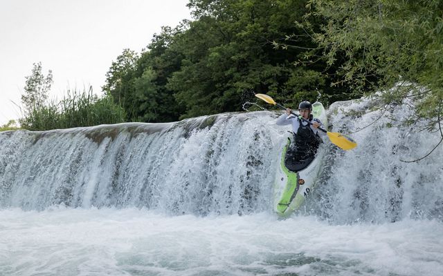 A person in a kayak goes over the edge of a short waterfall.